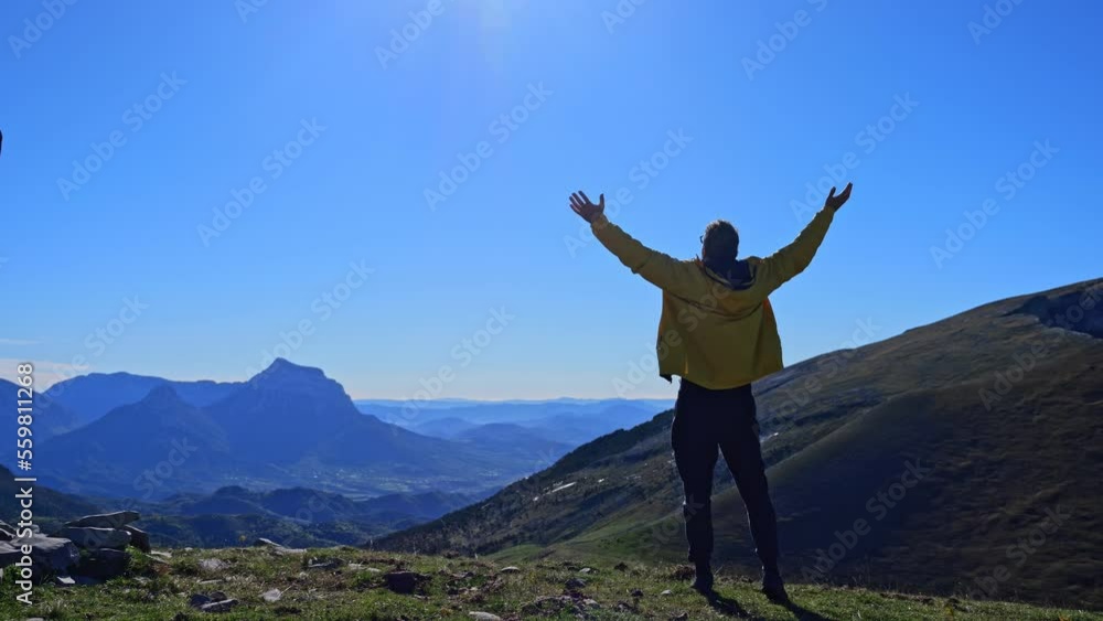Hipster millennial young man in a yellow jacket enters the frame against the backdrop of the mountain peaks, jumping on the rocks raising his hands in the air, happy and drunk with life and happiness Hipster millennial young man in a yellow jacket enters the frame against the backdrop of the mountain peaks, jumping on the rocks raising his hands in the air, happy and drunk with life and happiness