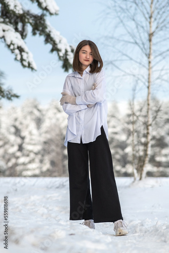 Portrait of a young beautiful girl of model appearance on a snowy field in winter in a net shirt and dark pants.