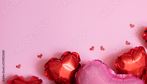 Valentines Day background with copy space and red heart shape small and big foil balloons on pink background flat lay
