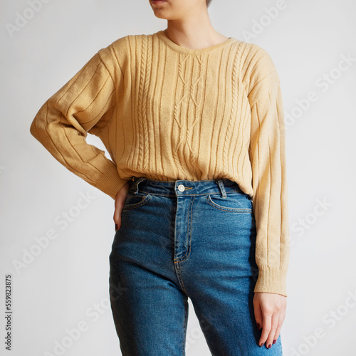 Woman wearing yellow sweater and blue mom jeans isolated on white background.