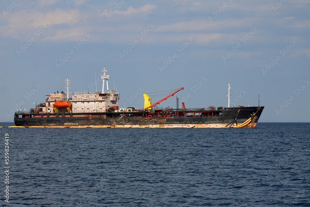 Huge black merchant ship is sailing on a blue boundless sea. A large vessel with a crane and antennas is sailing with cargo.