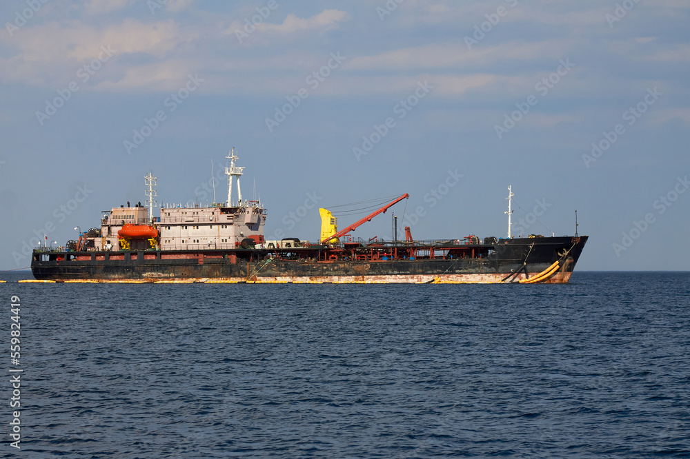 Huge black merchant ship is sailing on a blue boundless sea. A large vessel with a crane and antennas is sailing with cargo. Huge black merchant ship is sailing on a blue boundless sea. A large vessel with a crane and antennas is sailing with cargo.