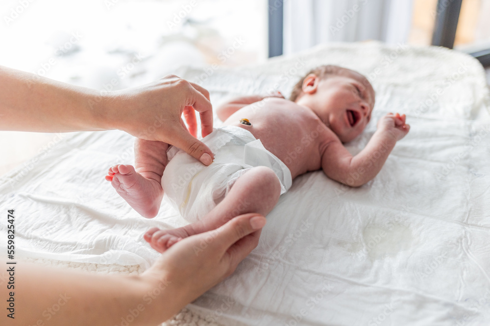 Newborn baby screaming while mother puts a diaper on the changing table