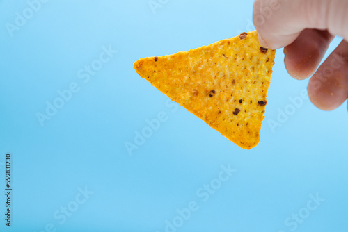 hand holding nachos chips isolated on blue background. chosing doritos