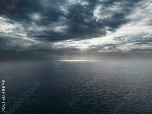 Aerial photo of a cloudy sky with sunbeams filtering and illuminating the surface of the calm sea of Palinuro. Photos of the Campania coast (southern Italy)