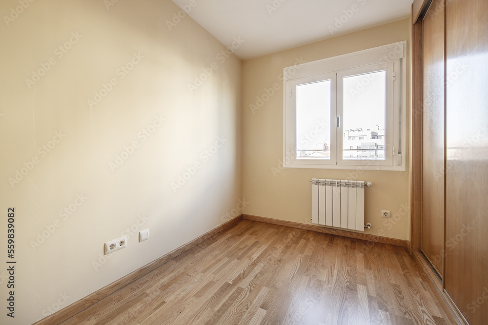 Room with a built-in wardrobe with three sliding oak doors with skirting boards and matching floors and smooth cream-colored walls and a white aluminum window with two hinged leaves Room with a built-in wardrobe with three sliding oak doors with skirting boards and matching floors and smooth cream-colored walls and a white aluminum window with two hinged leaves