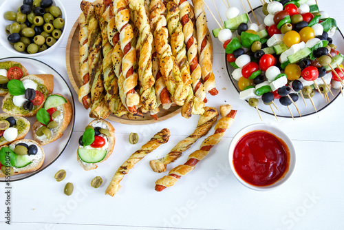 Snacks for the New Year's Eve party and carnival: sausages in puff pastry, puff pastry and pesto sticks, cheese and vegetable skewers, sandwiches and tomato sauce