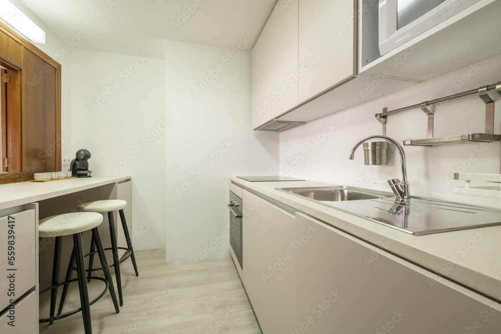 Modern handleless kitchen with sink with stainless steel single-lever faucet and worktop with serving hatch with matching stools Modern handleless kitchen with sink with stainless steel single-lever faucet and worktop with serving hatch with matching stools