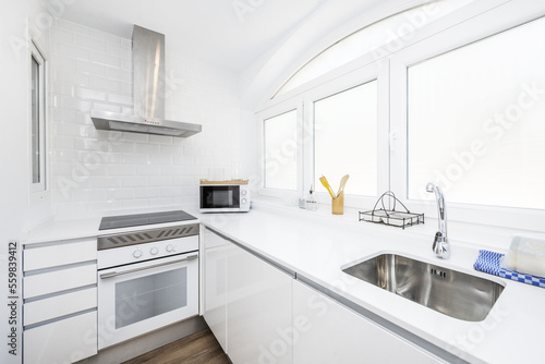 Corner of a kitchen with a large window  white stone countertops and cabinets  and built-in appliances