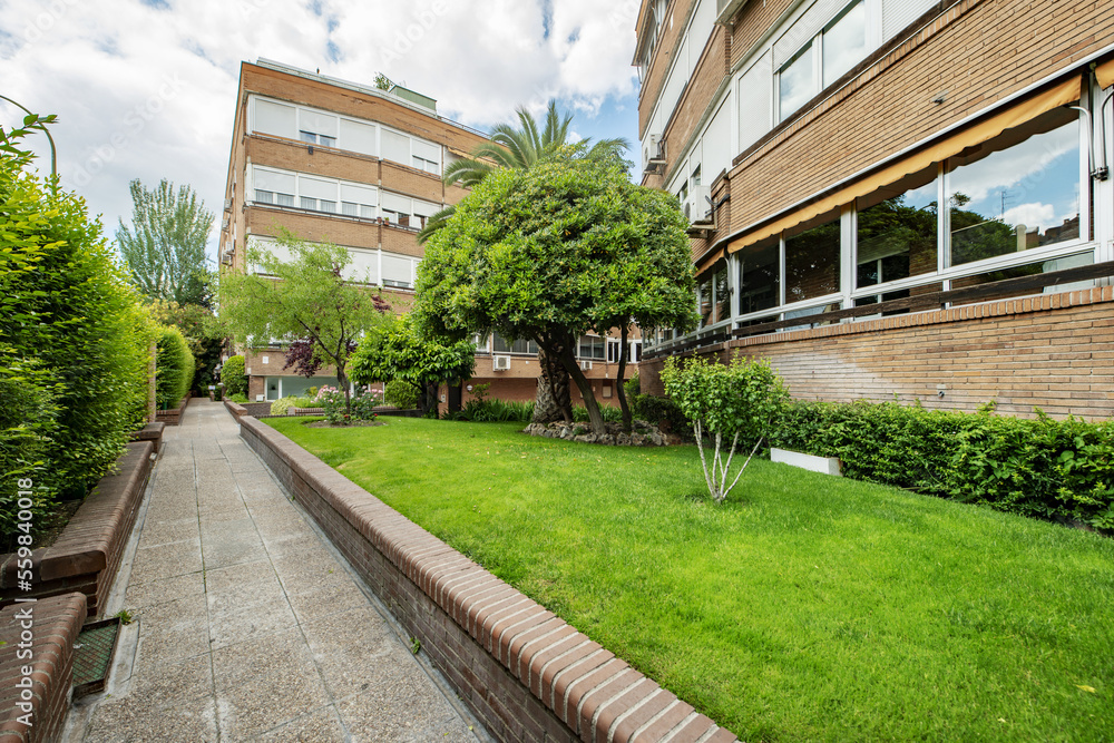Fototapeta premium Facade of a four-story building with white aluminum windows and walkways with lawn and tree-lined gardens