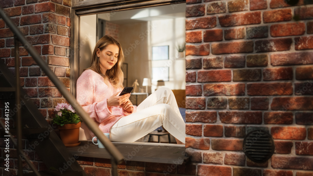 Woman in Pink Comfy Sweater Using Smartphone and Drinking Herbal Tea While Sitting on her Windowsill. Beautiful Housewife Enjoying her Alone and Wellbeing Time, Watching Tutorials on a Video Platform Woman in Pink Comfy Sweater Using Smartphone and Drinking Herbal Tea While Sitting on her Windowsill. Beautiful Housewife Enjoying her Alone and Wellbeing Time, Watching Tutorials on a Video Platform