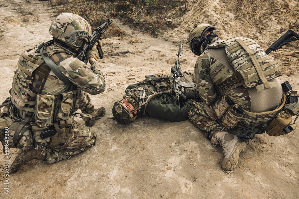 Fototapeta premium Wounded man lying on a ground, other soldiesr next to him
