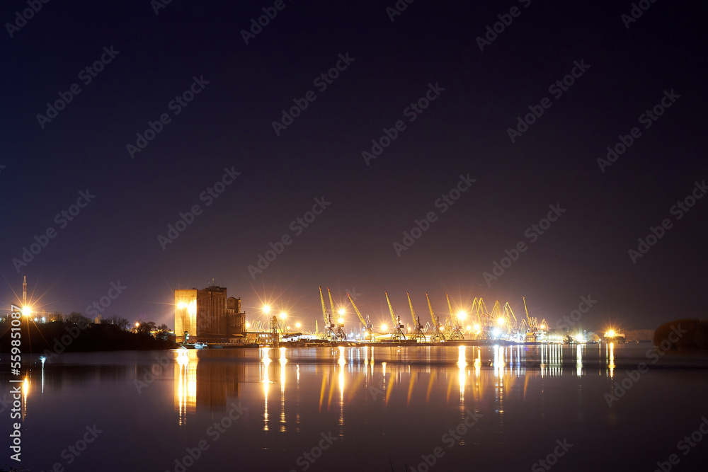 Night scene of river port cranes with reflections on the water. Cargo Port at Night