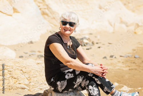 Old woman in black clothes sitting on a rock near the sea and having fun. Happy retirement time
