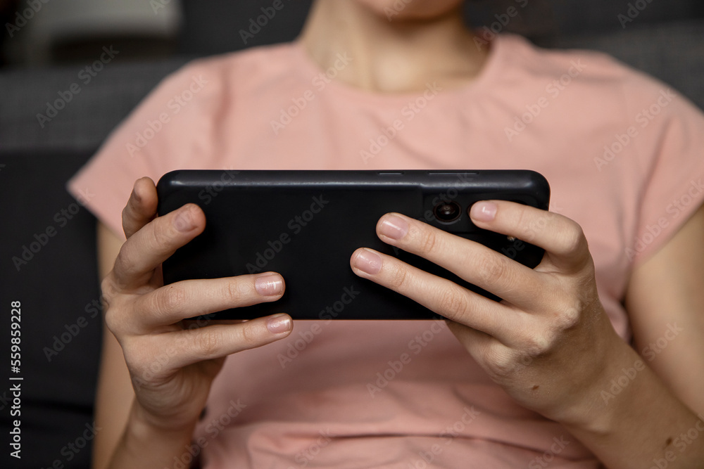 A teenage girl using a smartphone, presses her finger, reads social networks on the Internet, types text or plays video games, a mobile phone in two hands close-up A teenage girl using a smartphone, presses her finger, reads social networks on the Internet, types text or plays video games, a mobile phone in two hands close-up