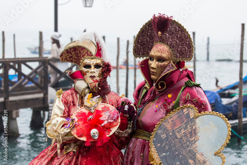 coppia di maschere di carnevale in posa davanti a gondole ormeggiate, taglio orizzontale