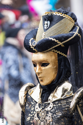ritratto a tre quarti di maschera di carnevale di venezia, maschera dorata, cappello con velo, ricami e disegno in oro su sfondo blu scuro