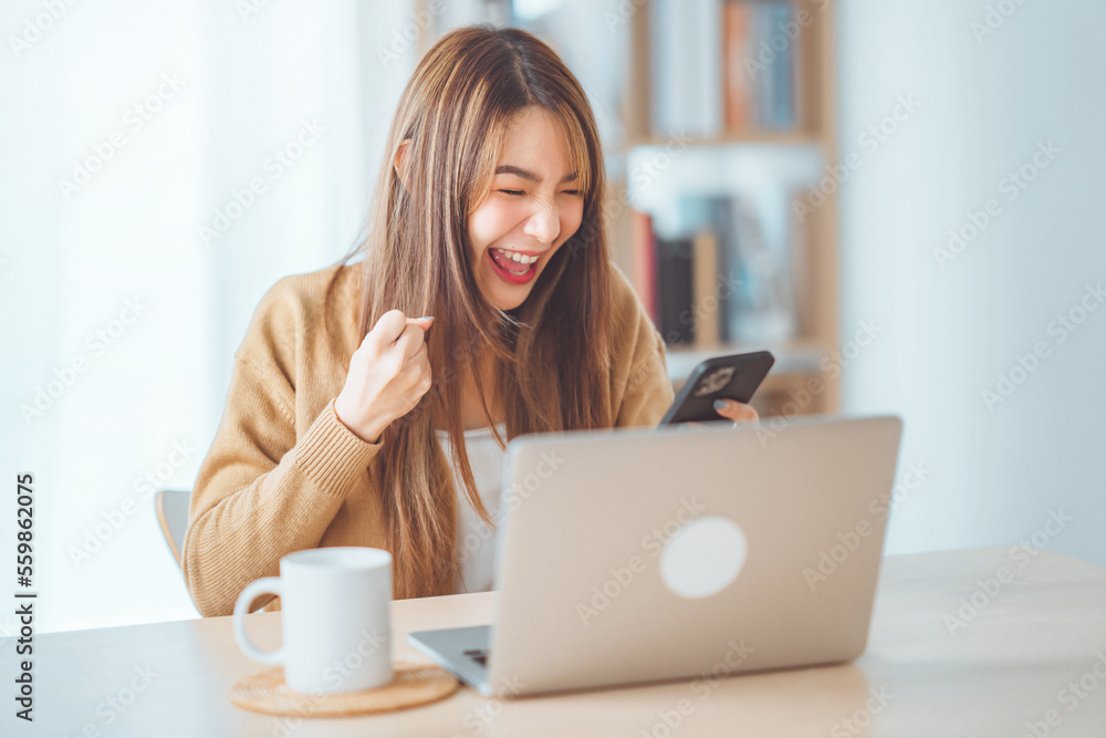 Excited young asian woman winner looks at laptop celebrates online work at home on desk with successful. Reads good news in email, Achieve target project.