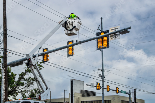 Worker up high in crane bucket repairing traffic light at city intersection on cloudy day with building in background