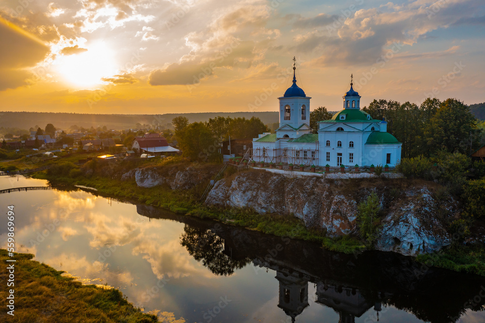sunset with the rays of the sun on the background of the domes of the temple on the rock by the river, a beautiful view of the village in Russia