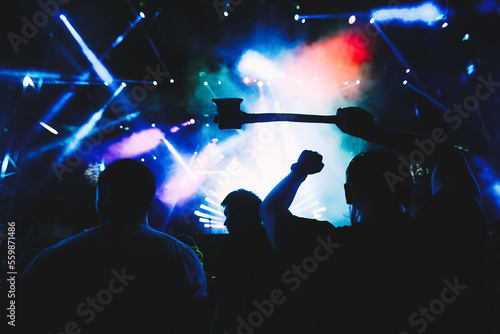 Photo of young people having fun at rock concert. Fans applauding to famous music band. DJ on a stage in the club. Crowd dancing on dance-floor.