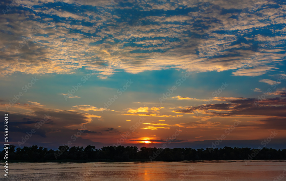 Beautiful sunset with clouds and the setting sun under the horizon over the forest and the river