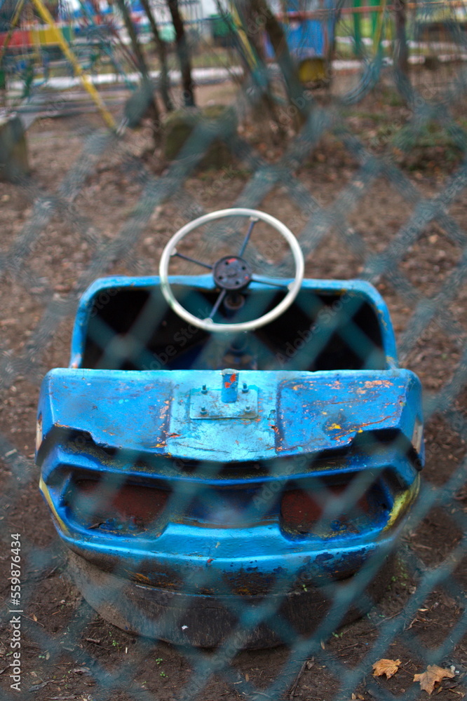 Old bumper car with cracked paint behind a metal mesh fence in an abandoned amusement park
