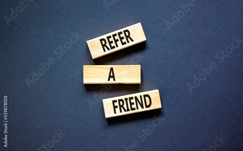 Refer a friend symbol. Concept words Refer a friend on wooden blocks on a beautiful black table black background. Business and refer a friend concept. Copy space.