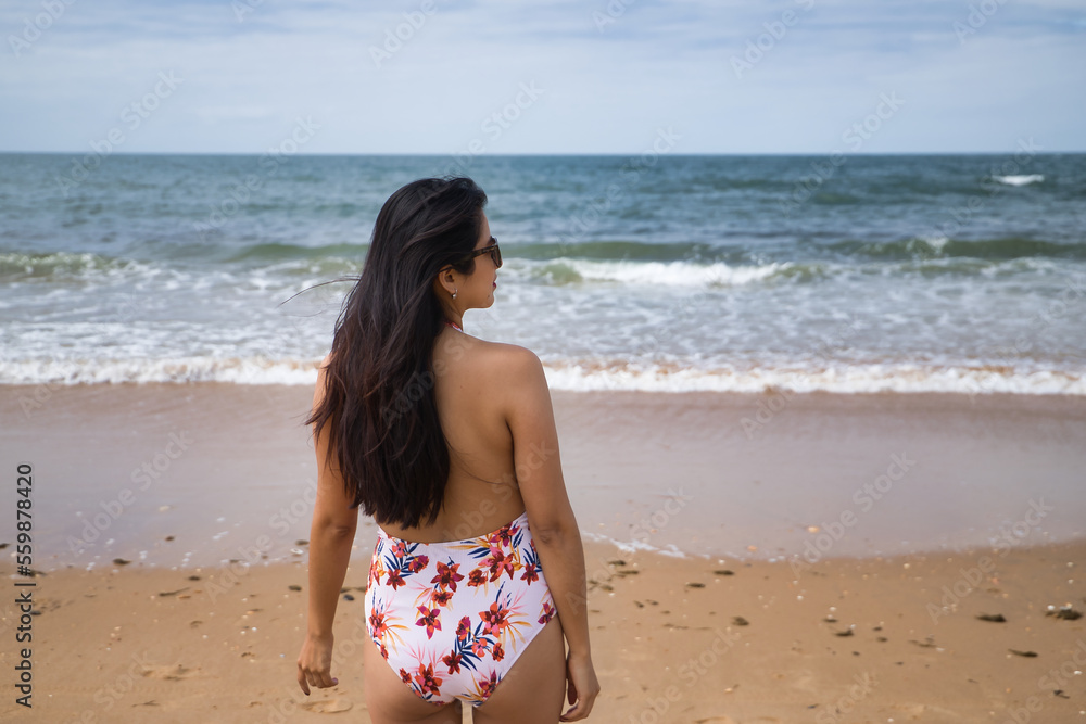 South American woman, young and beautiful, brunette with swimsuit on her back looking at the sea. Concept sea, sand, sun, beach, vacation, travel, summer. South American woman, young and beautiful, brunette with swimsuit on her back looking at the sea. Concept sea, sand, sun, beach, vacation, travel, summer.