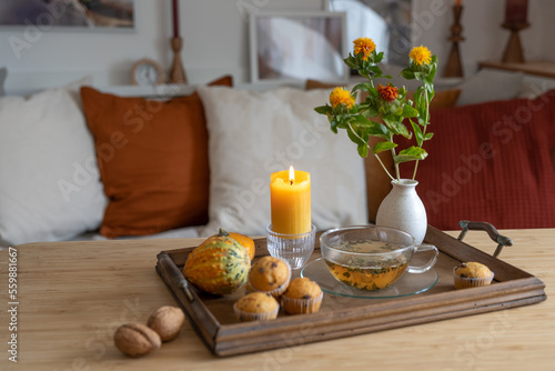 Tray with a cup of tea, lit candle and autumn decoration on a table in the living room, cozy home in the cold season, copy space, selected focus