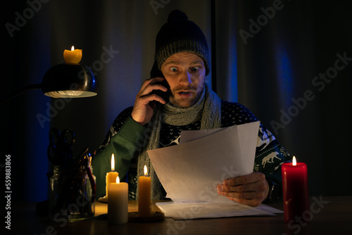 Schilderij op canvas shocked man in candle light looking at high bills for electricity, gas heating in cold dark room at home