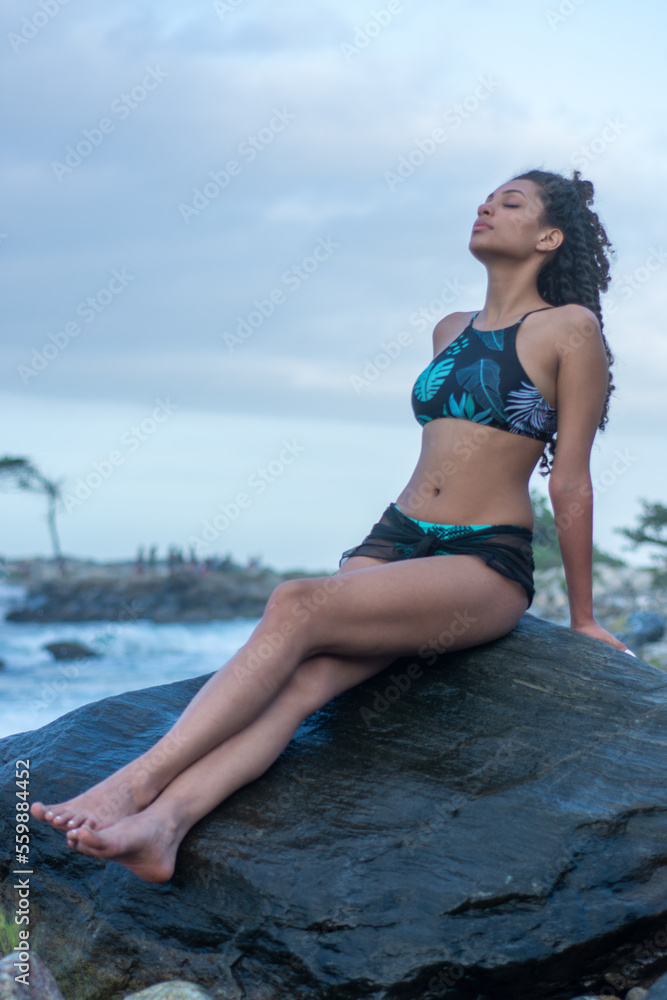 girl in a bathing suit sitting on a rock breathing with her eyes closed in the ocean girl in a bathing suit sitting on a rock breathing with her eyes closed in the ocean