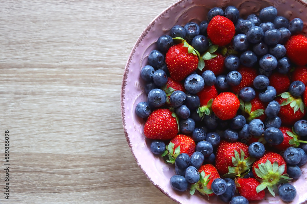 Pink rustic bowl filled with fresh blueberries and strawberries. Wooden background, top view. Pink rustic bowl filled with fresh blueberries and strawberries. Wooden background, top view.