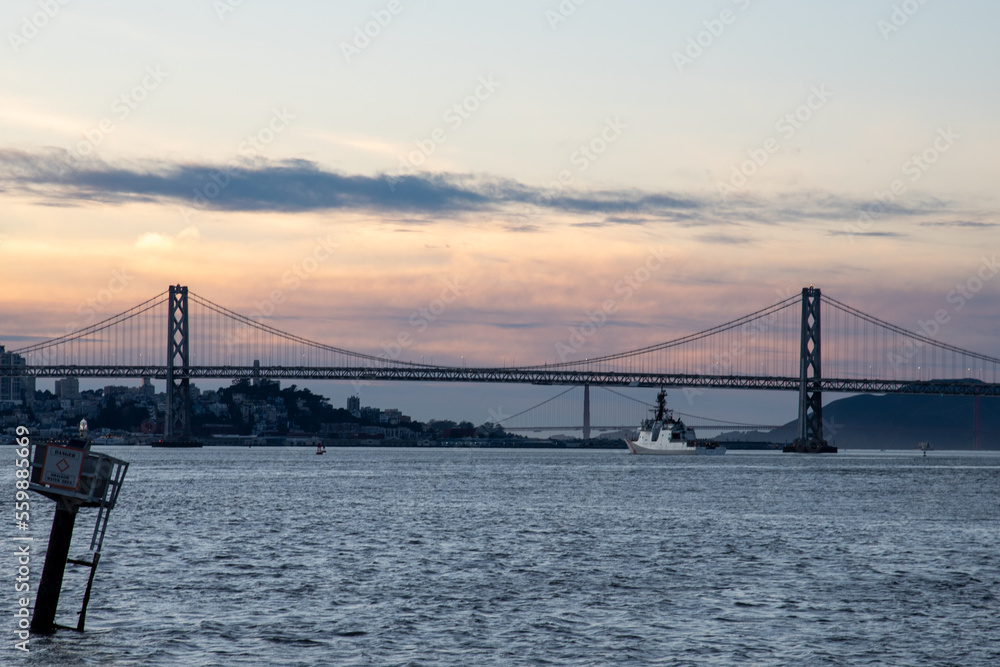 ship traveling under bay bridge at sunset with Golden Gate in background ship traveling under bay bridge at sunset with Golden Gate in background