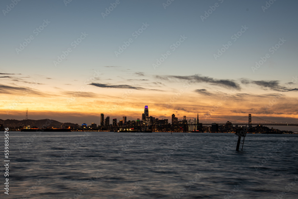 sunset behind San Francisco skyline across bay with buildings lit and bridge