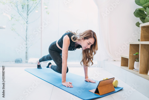 beautiful woman exercise watching tablet online in living room. gorgeous determined woman on yoga mat looking at guide online. motivated beautiful woman gaining body burn watching tutorial on tablet photo