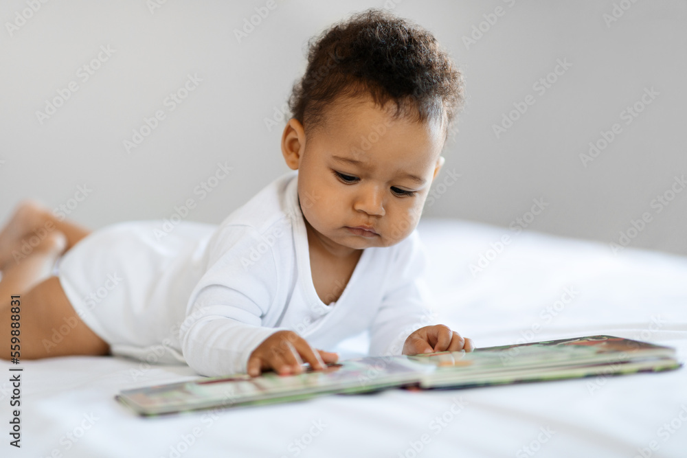 Adorable Black Baby Looking At Pictures In Book While Relaxing In Bed Adorable Black Baby Looking At Pictures In Book While Relaxing In Bed