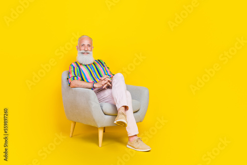 Full size portrait of cheerful aged man sitting armchair have good mood isolated on yellow color background