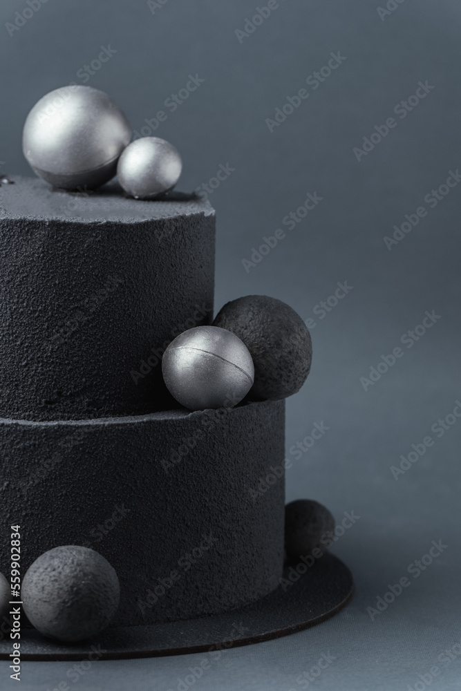 Anniversary luxury black bunk cake with chocolate velvet coating on dark grey background. Birthday cake with black velvet texture decorated with silver chocolate spheres