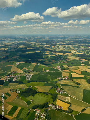 View from airplane of countryside land and property near Munich, Germany. Beautiful patchwork design is seen underneath a sky of fluffy clouds.
