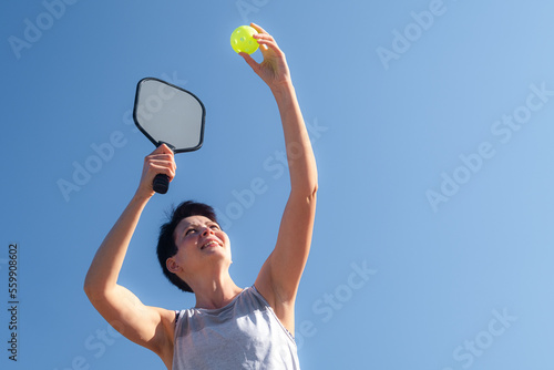 woman playing pickleball game, hitting pickleball yellow ball with paddle, outdoor sport leisure activity.