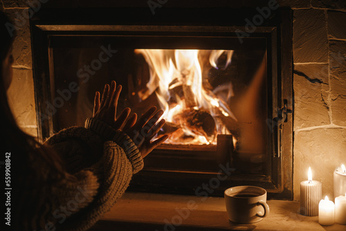 Foto Woman hands warming up at cozy fireplace in dark evening room, close up