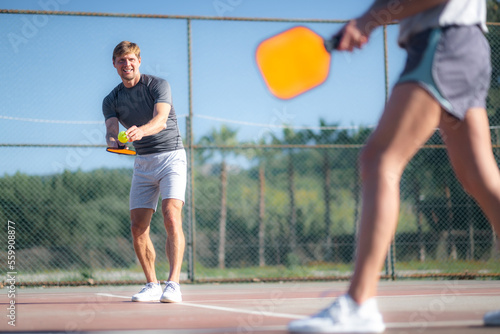 couple playing pickleball game  hitting pickleball yellow ball with paddle  outdoor sport leisure activity.