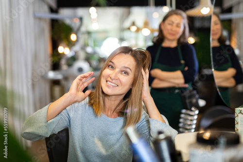 Young woman approving result of hairdresser work, looking satisfied with new hairdo.