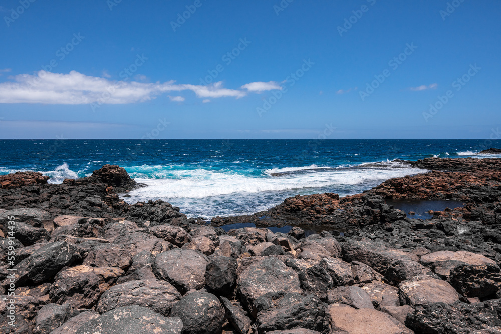 Wild rocky coastline of Fuerteventura, Canary Islands, Spain. A big wave crashes on the rocks in rocky bay. Squirrels hiding among the rocks. Turquoise colors.