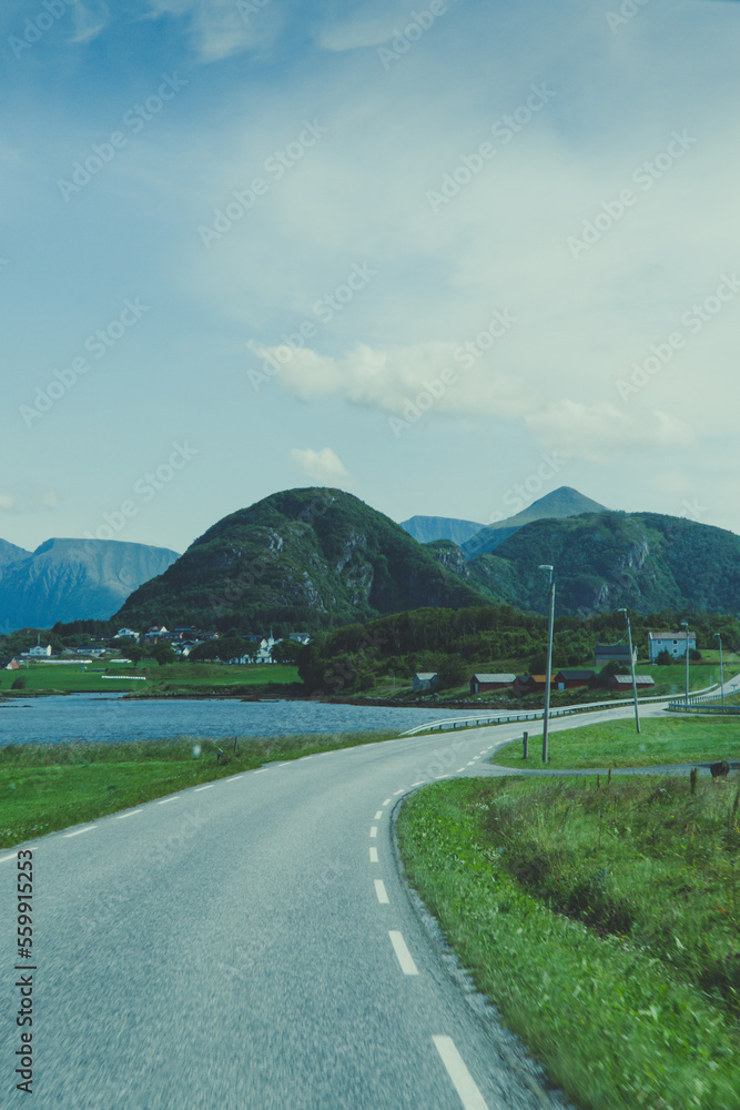 The road leads into the mountains past a lake and a village