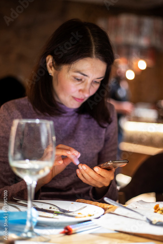 beautiful brunette girl in a lilac sweater writes sms in a gadget in a cafe. A party