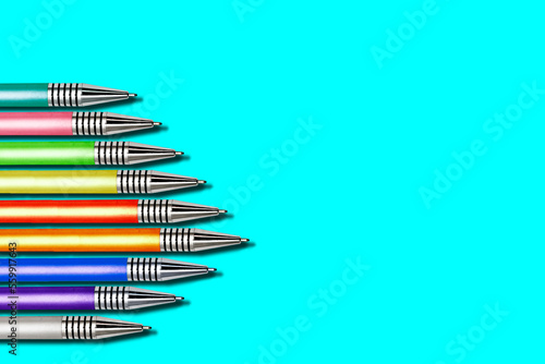 Multi-colored ballpoint pens in a row on a light background