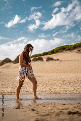 chica paseando por el agua con vestido de flecos y pelo largo suelto.