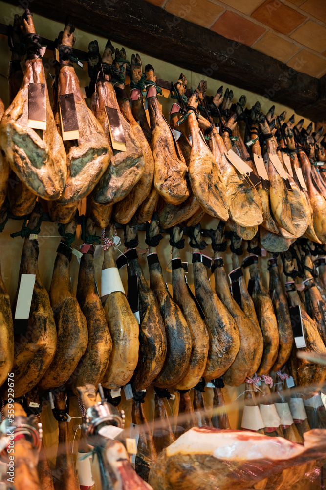 Abundance of dry-cured pig's legs in spanish jamoneria. Lots of preserved pork meat at counter in market.